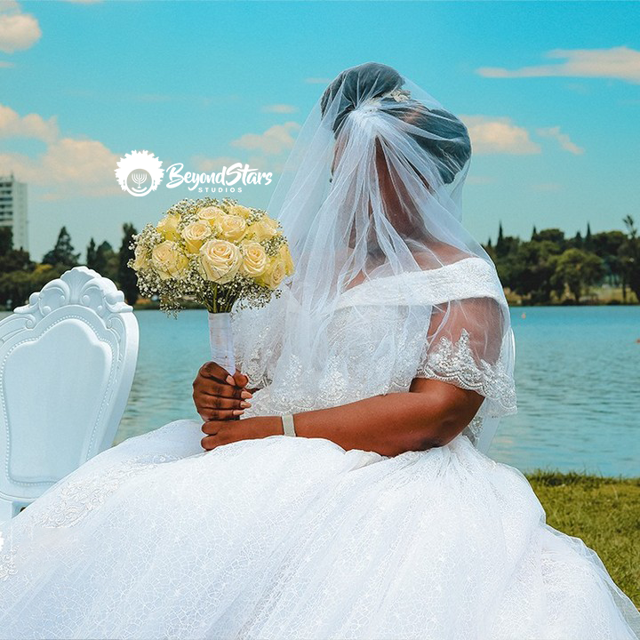 Bride in a lace gown holding yellow roses by the lake